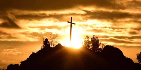 Uma cruz no alto de uma montanha contra um pôr do sol avermelhado e dourado